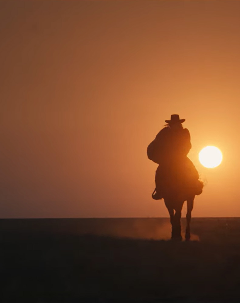 Cowboy riding in front of a sunset.