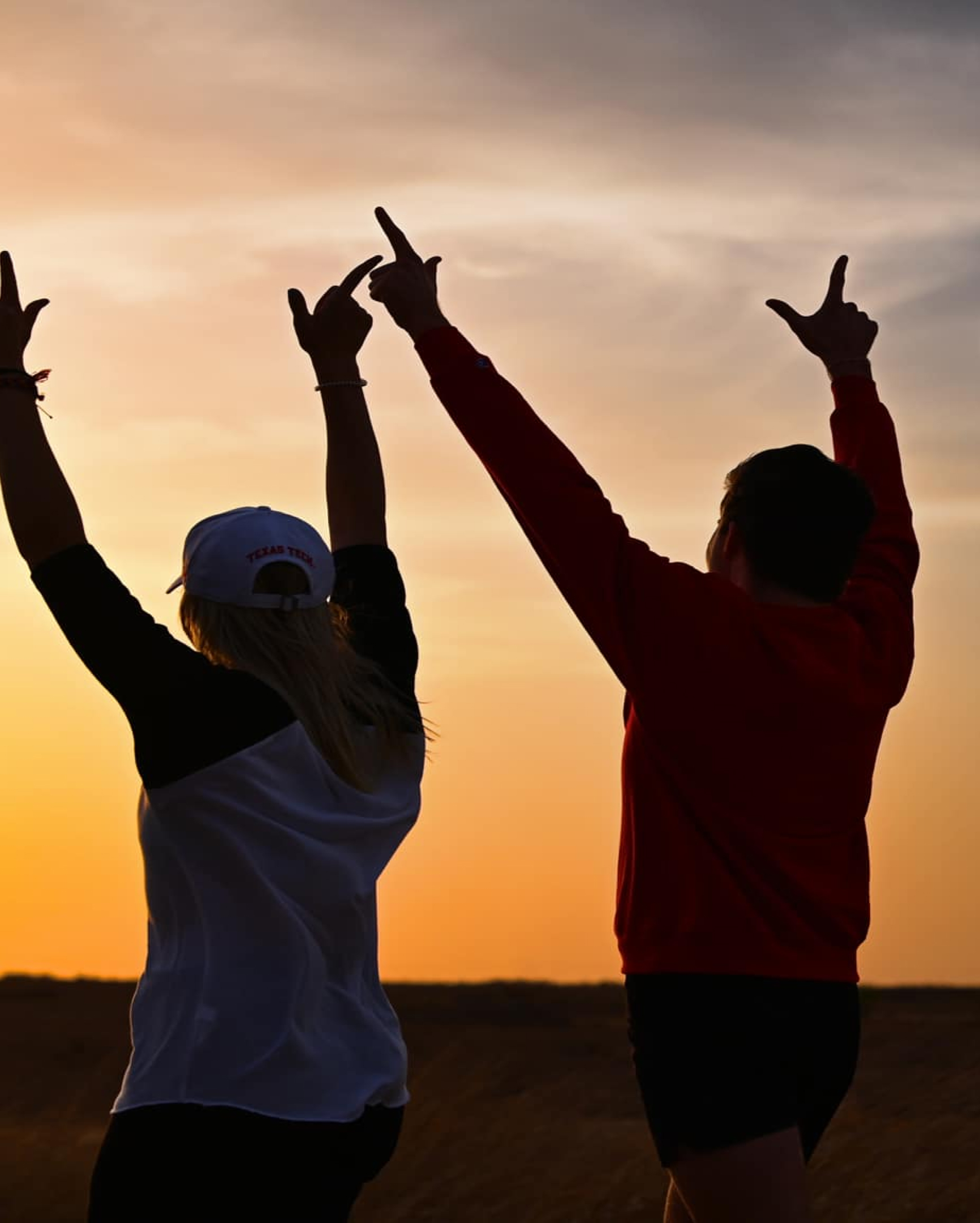 Two people walking at sunset with their hands in the air.