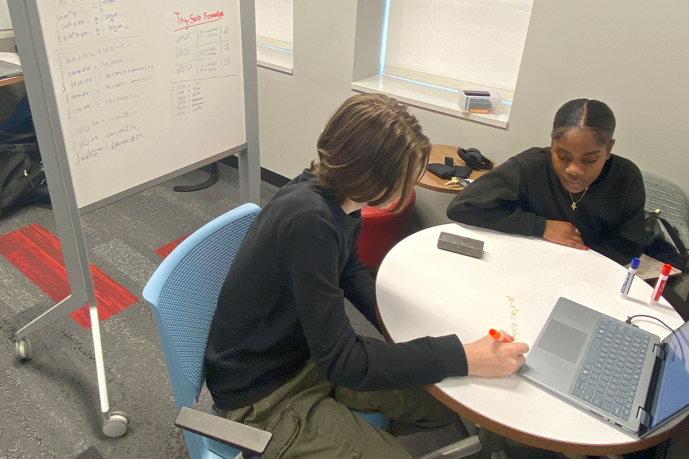 Students sitting at a table with a laptop and a dry erase board nearby. 