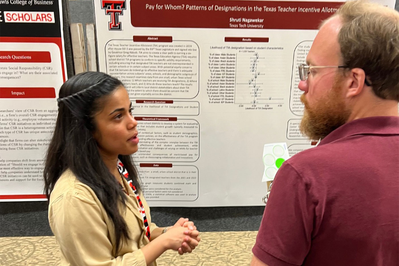 Shruti talks with a man while standing in front of her research poster. 